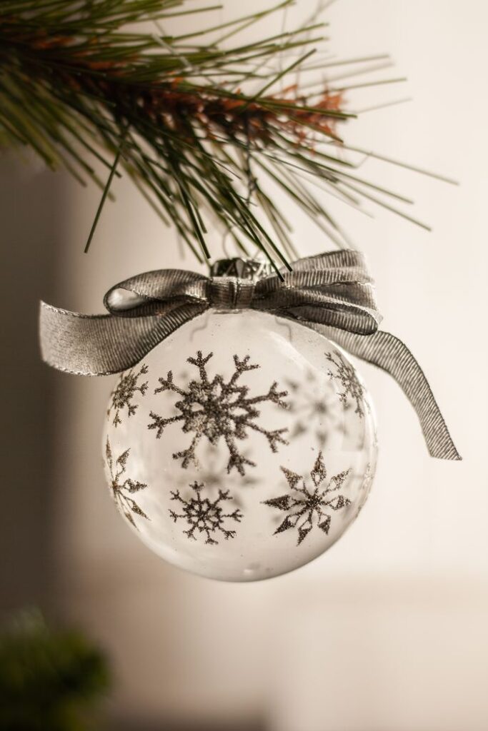 Close-up of a silver Christmas ornament with snowflake designs hanging from a tree branch.