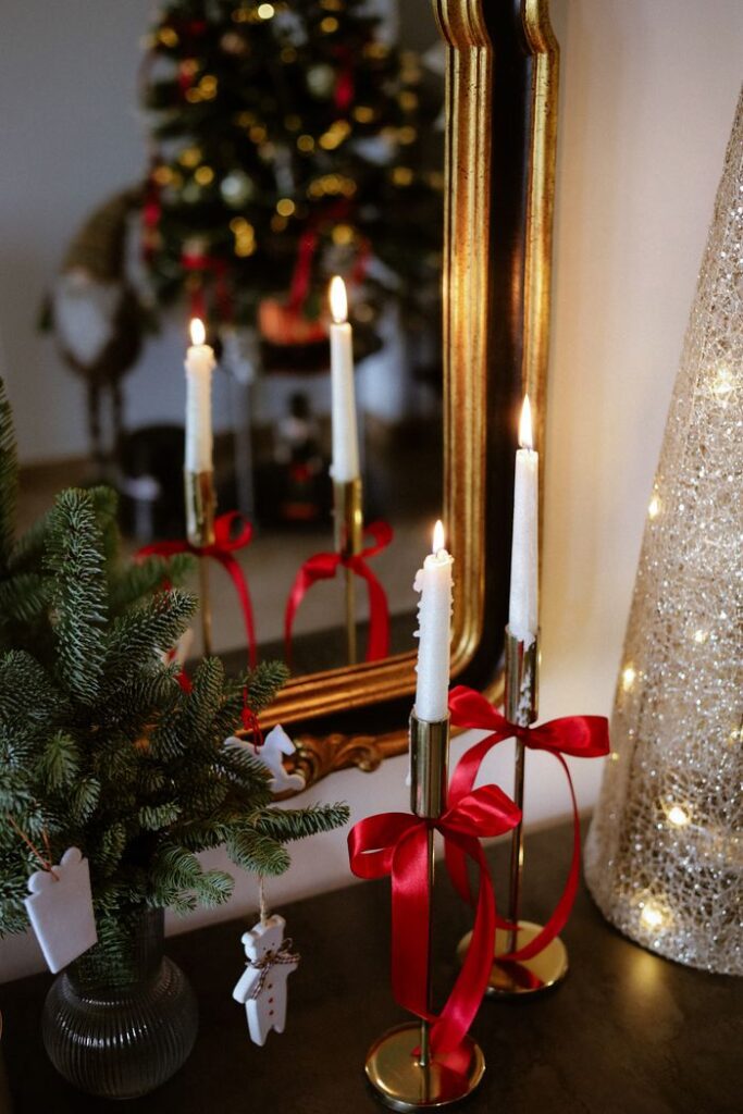 Elegant Christmas candle setup with red ribbons and mirror reflection for a cozy holiday atmosphere.