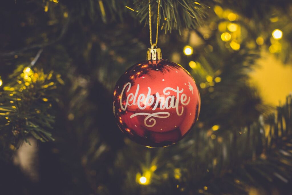 Close-up of a red Christmas ornament with 'Celebrate' text hanging on a decorated tree branch.